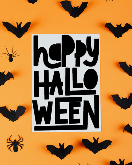 Greeting card with bold 'happy HALLO WEEN' text, bats, spiders, and orange background.
