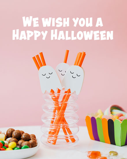 Cute ghost figures on orange straws in a vase with candy around.