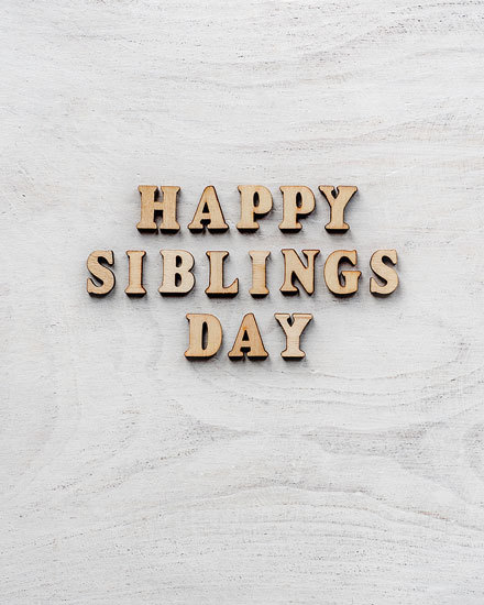 Rustic wooden letters on white background spell 'Happy Siblings Day'.