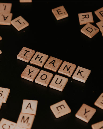 Wooden letter tiles spelling 'THANK YOU' on dark background.